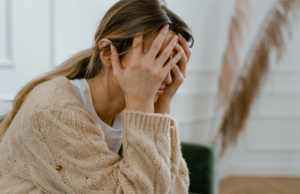 frustrated puppy owner sitting on a couch, visibly exasperated. The owner has their hands on their head, showcasing a sense of overwhelm. In the background, the room is cluttered with chewed-up shoes and torn pillows, indicative of the challenges faced in puppy training. This image represents the theme of the blog post, "Why Saying 'No' is Not Effective in Puppy Training," highlighting the struggles and frustrations that arise when traditional negative reinforcement methods fail to produce desired results.